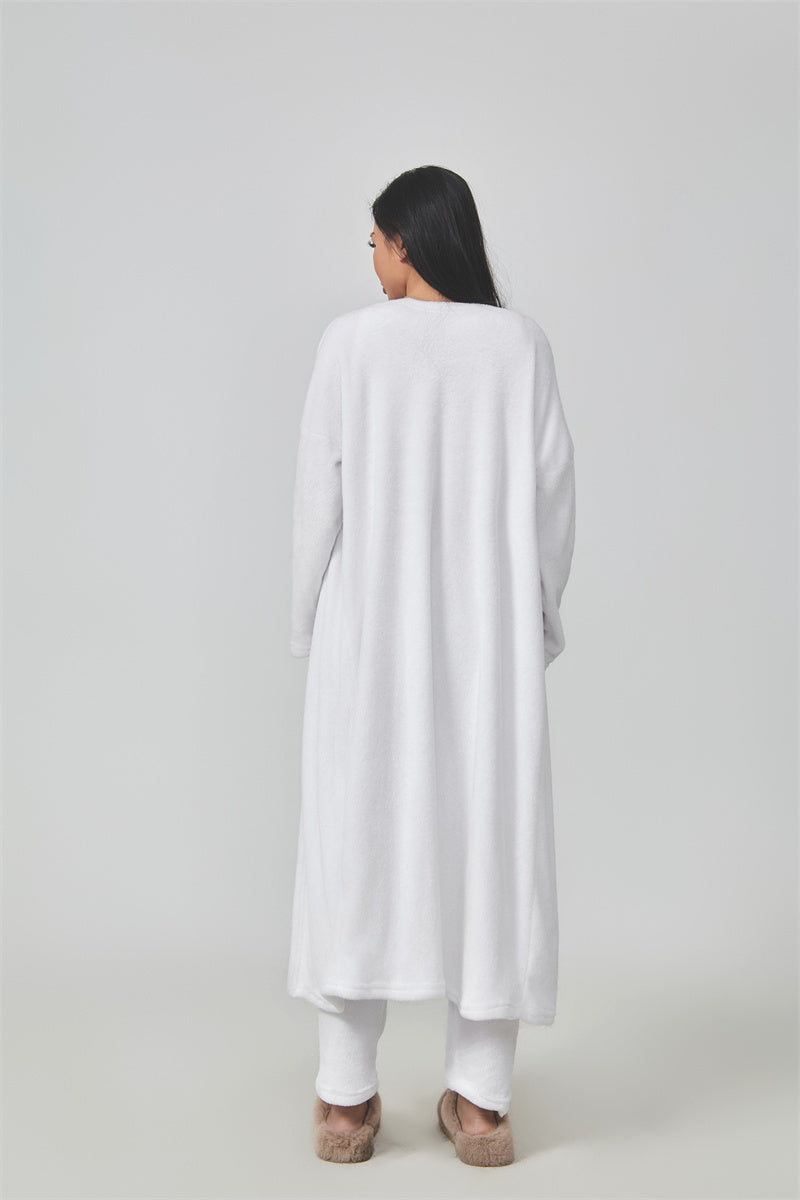 Woman wearing a long white cardigan over a white outfit on a light gray background