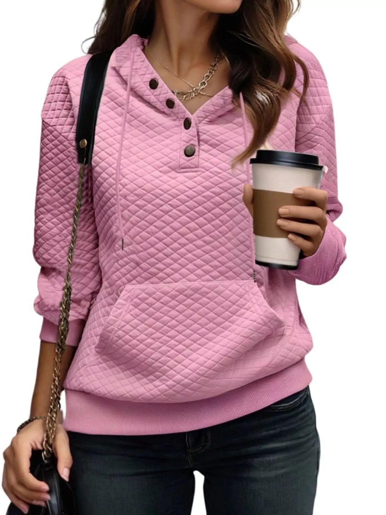Person wearing a pink quilted hoodie holding a coffee cup on a white background
