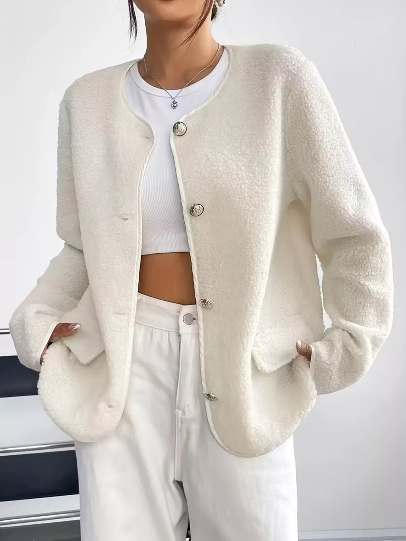 Person wearing a cream-colored cardigan over a white top and pants against a plain background