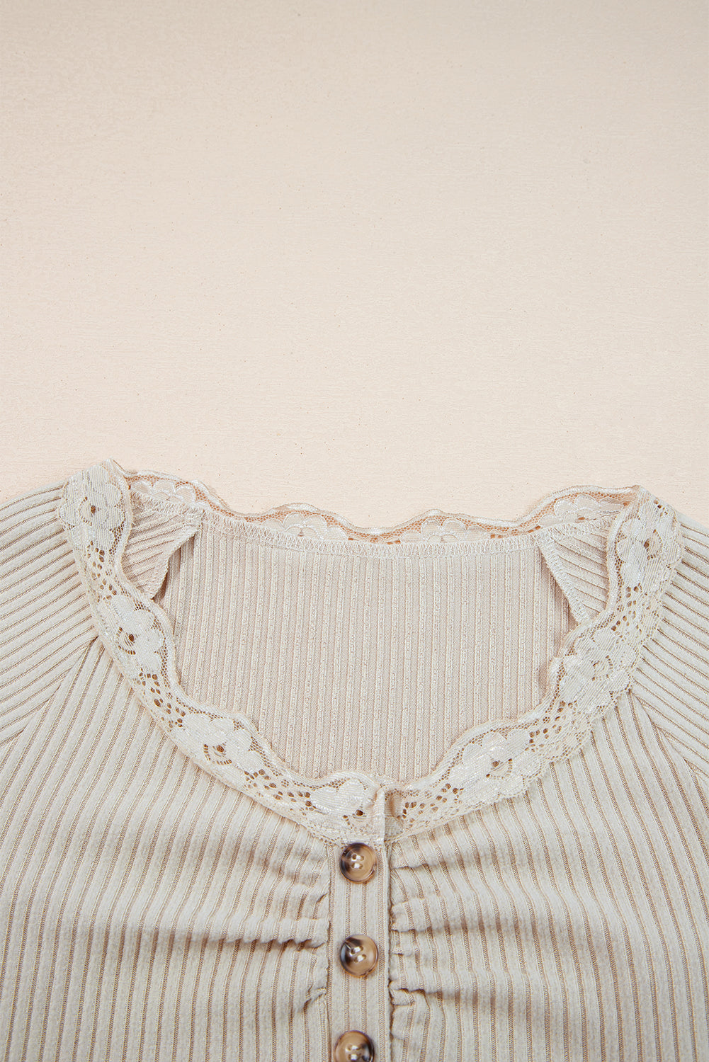 Close-up of a ribbed sweater with lace detailing and buttons on a beige background