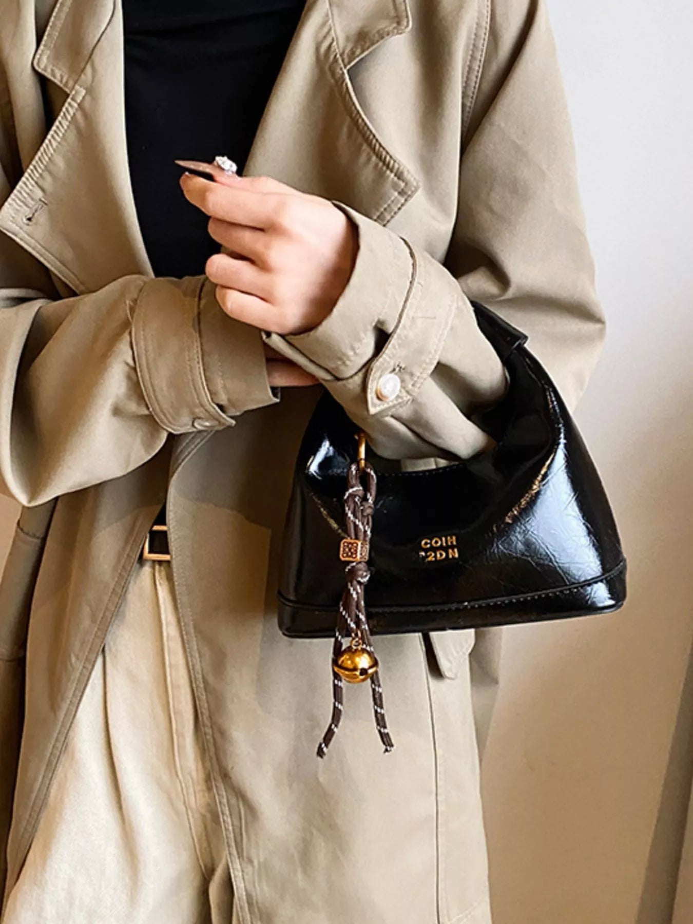 Person holding a black handbag with visible brand name, wearing a beige coat.
