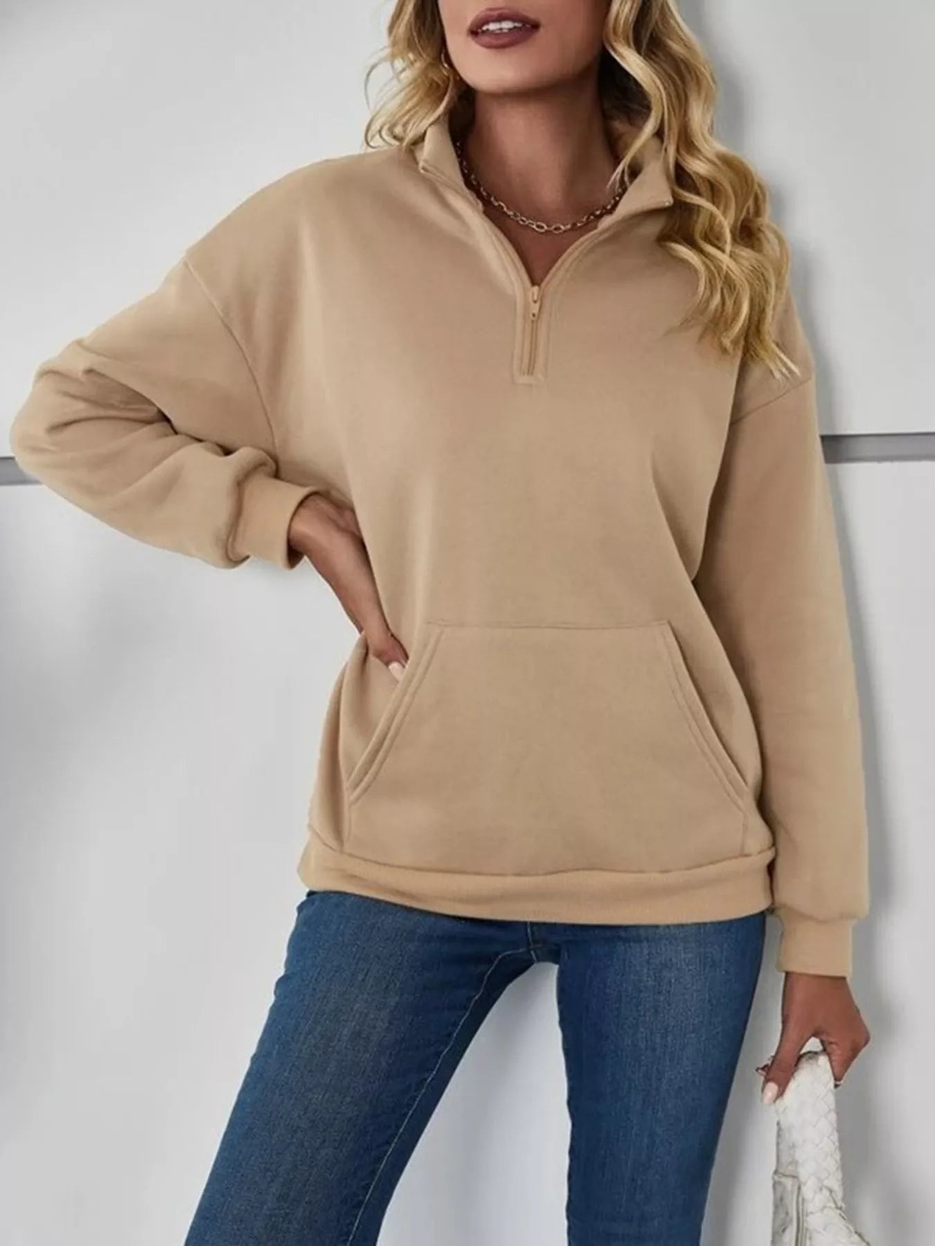 Woman wearing a beige pullover with a quarter zip and blue jeans on a white background