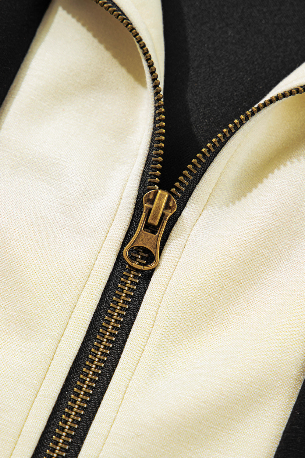 Close-up of a gold zipper on a cream jacket with black accents