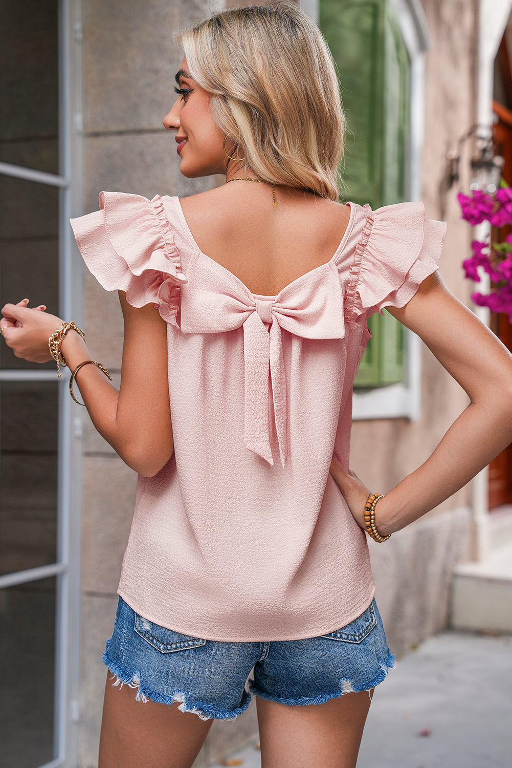 Woman wearing a pink blouse with ruffled sleeves and a bow at the back, standing outdoors.