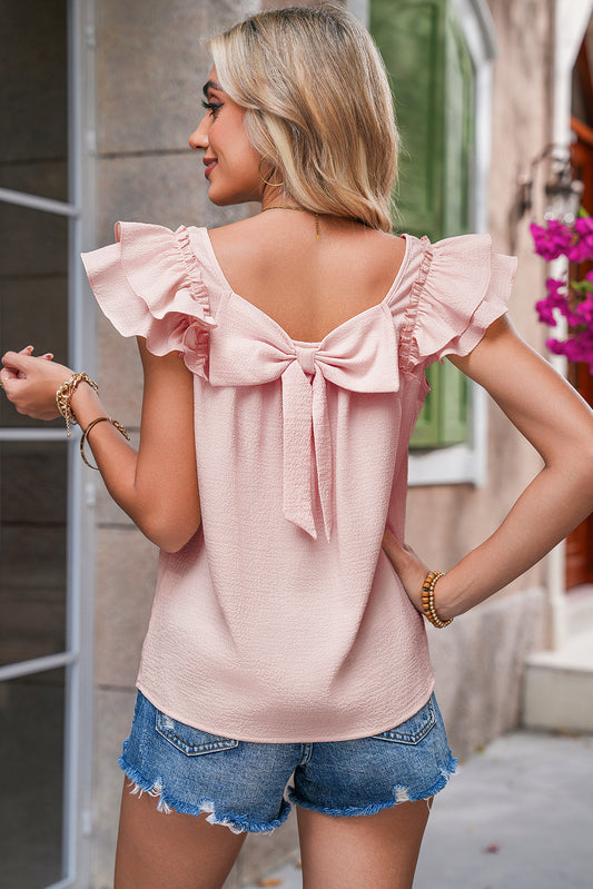 Woman wearing a pink blouse with ruffled sleeves and a bow at the back, standing outdoors.