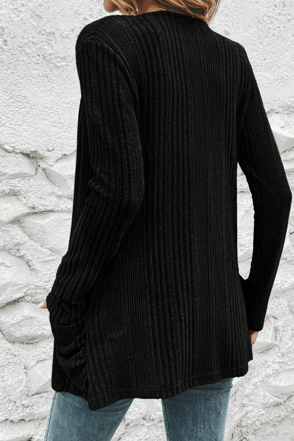 Person wearing a black ribbed sweater against a stone wall background