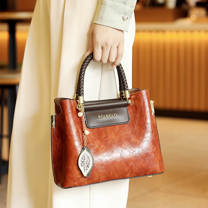 Brown handbag with gold accents held by a person in a blurred indoor setting