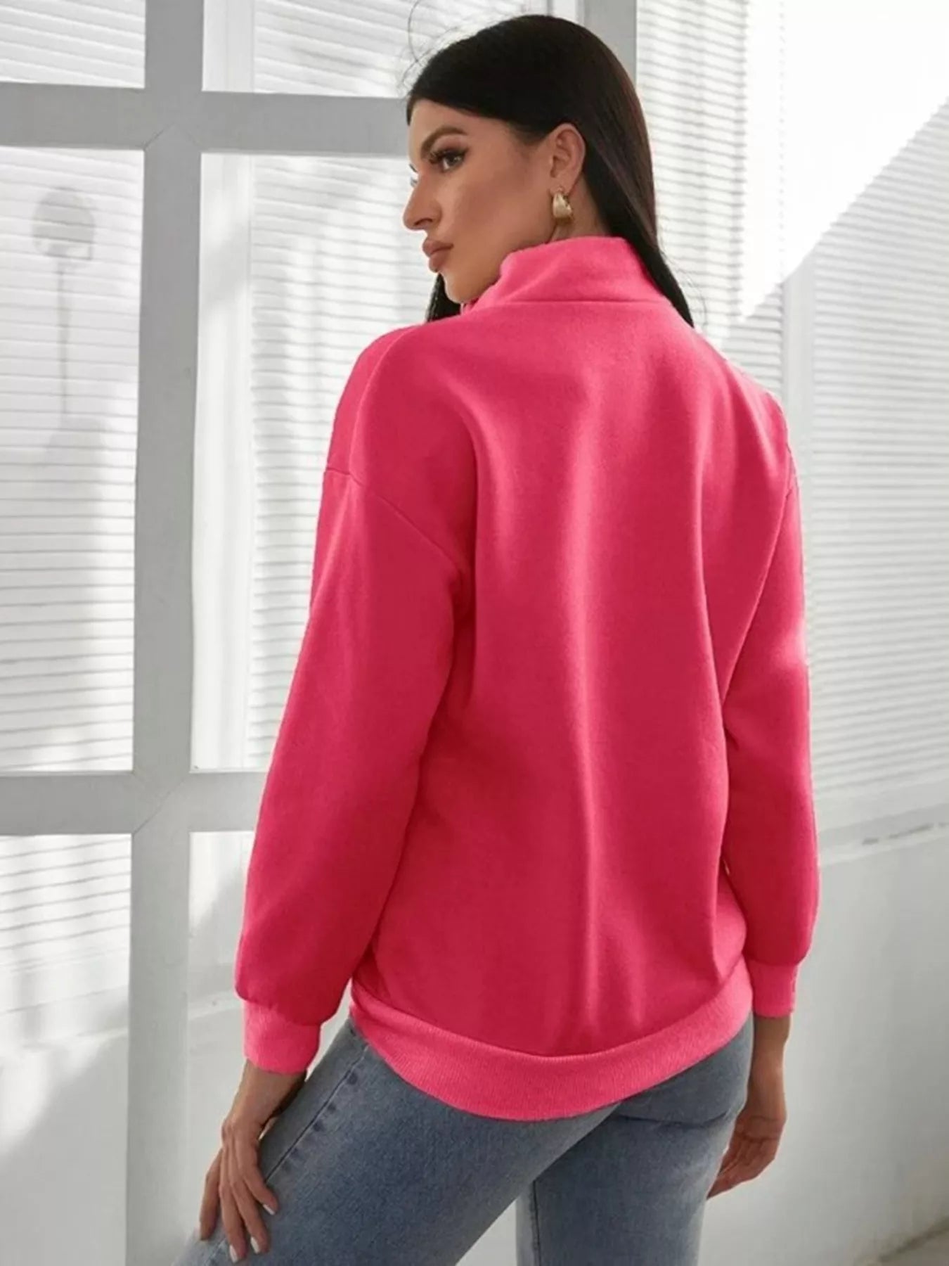 Person wearing a bright pink jacket in front of a window with blinds.