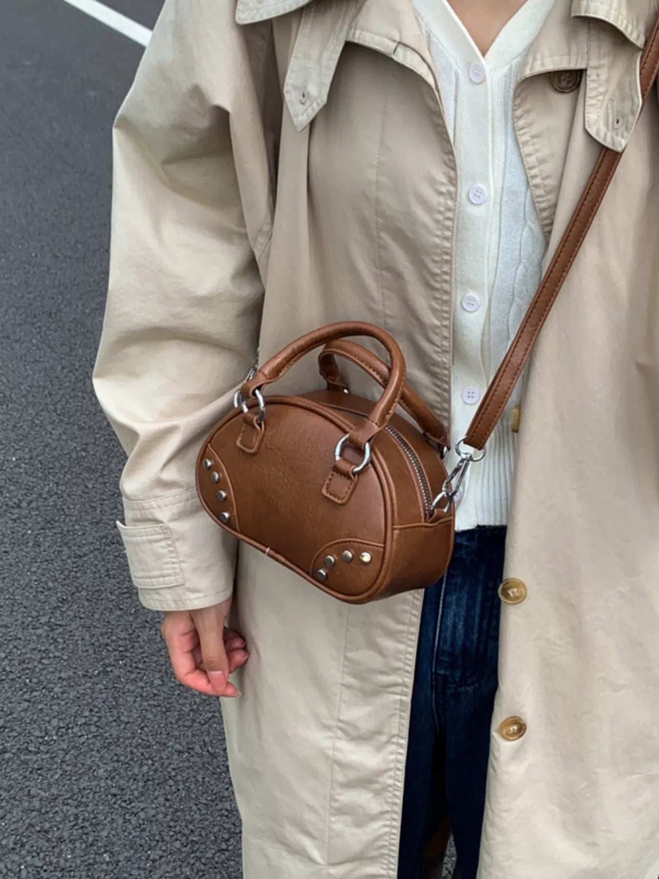 Person wearing a beige trench coat holding a brown handbag on a street.