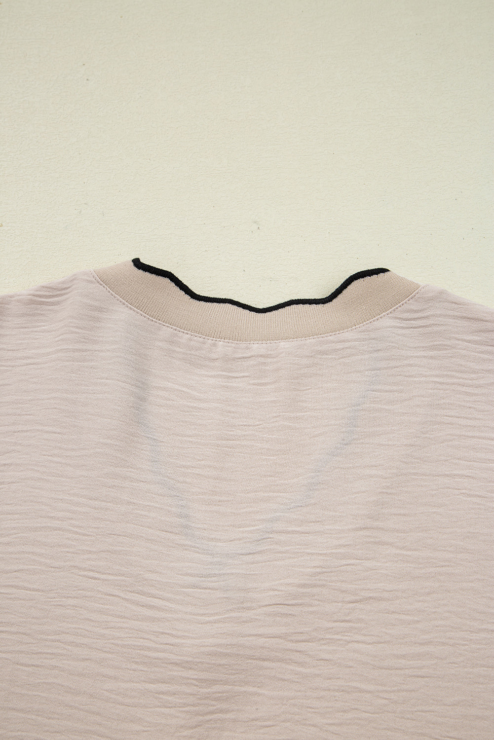 Light pink shirt with black trim on a beige background