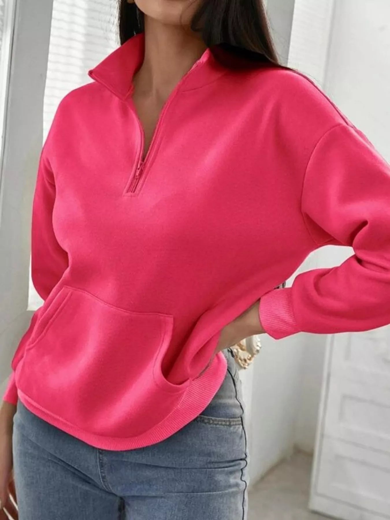 Person wearing a bright pink long-sleeve top with a zipper, standing indoors.