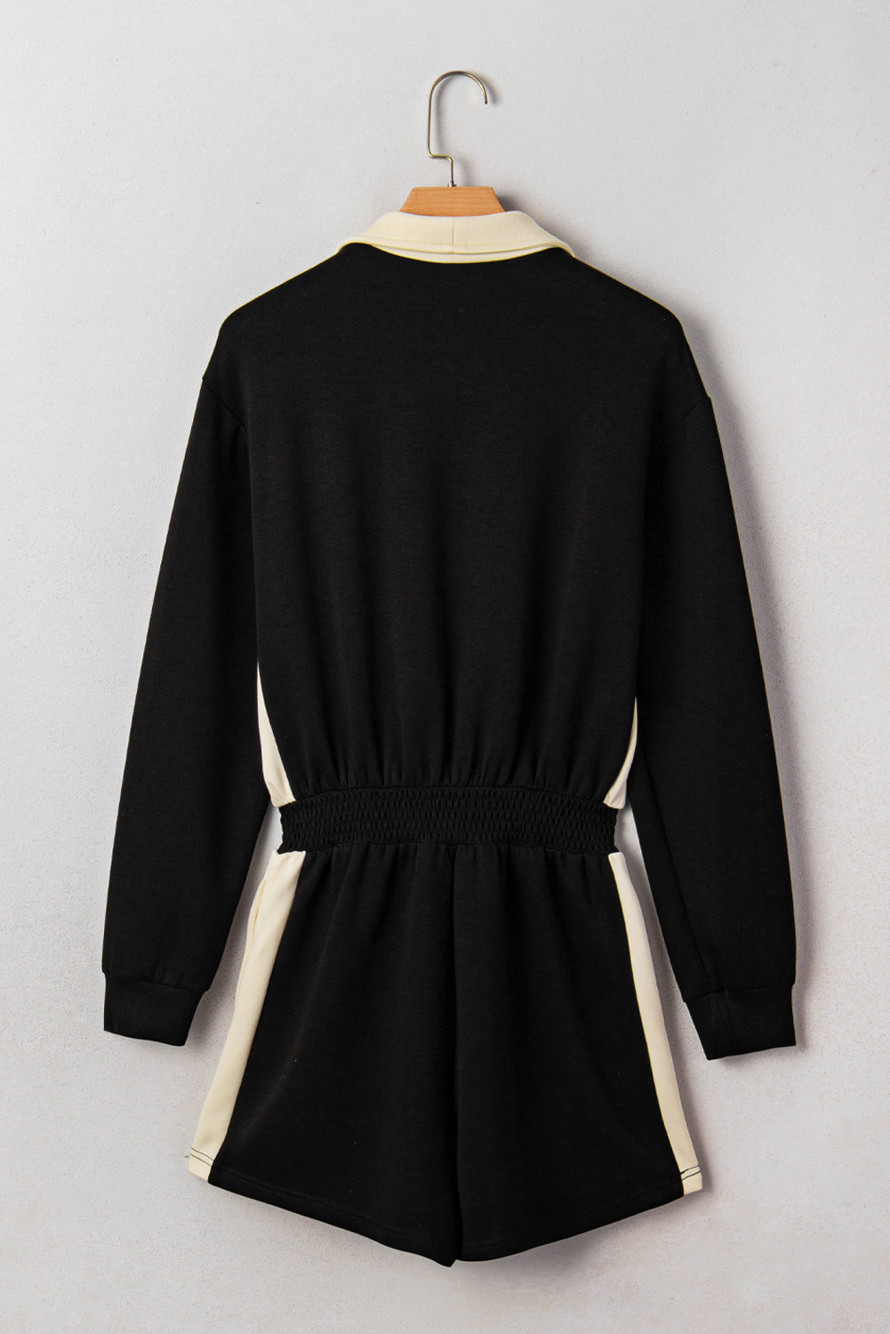 Black dress with white trim on a hanger against a light gray background