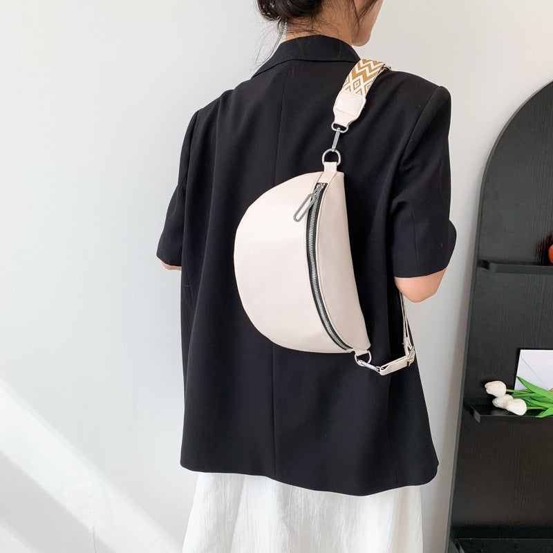 Person wearing a black shirt with a white round bag on a plain background