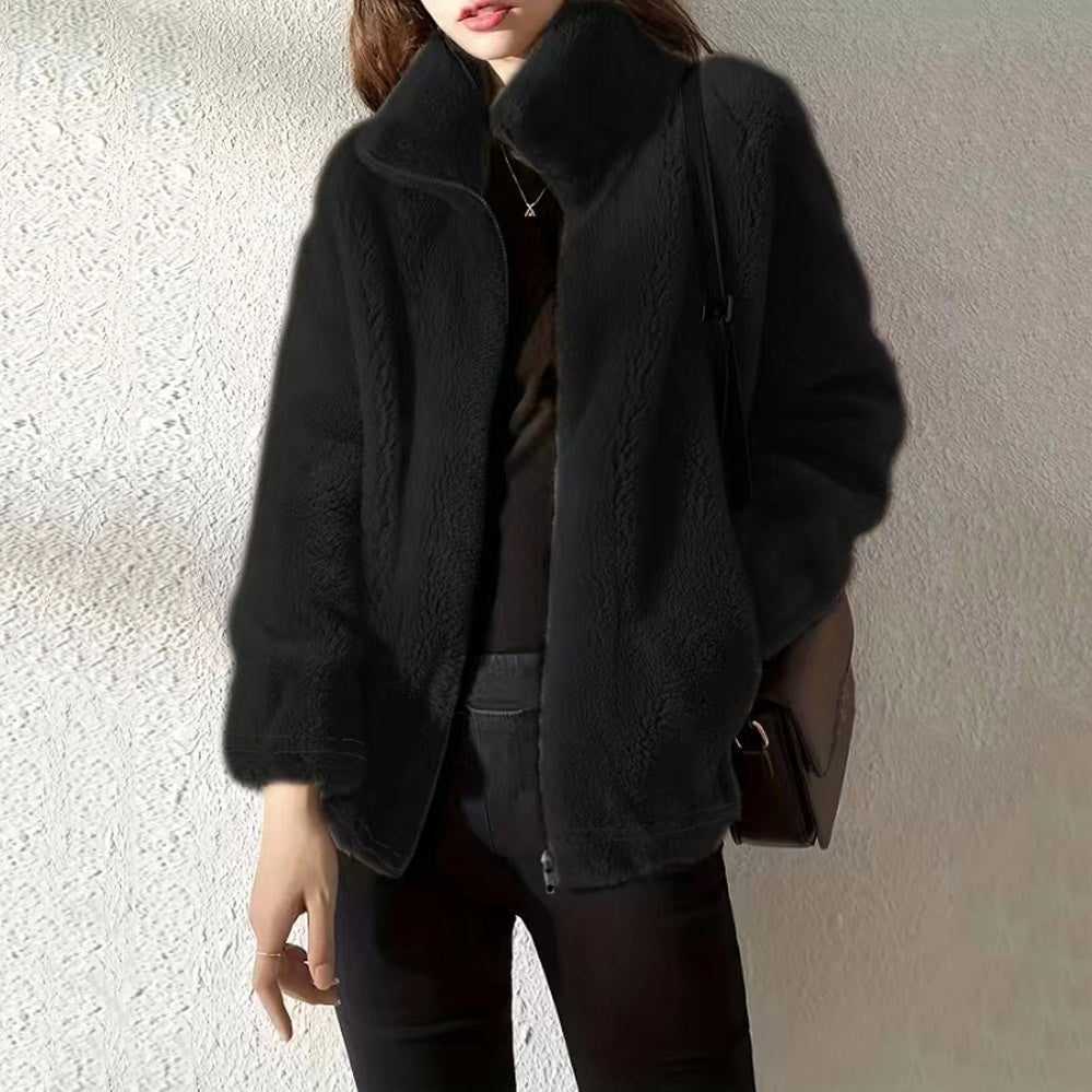 Person wearing a black coat against a neutral background