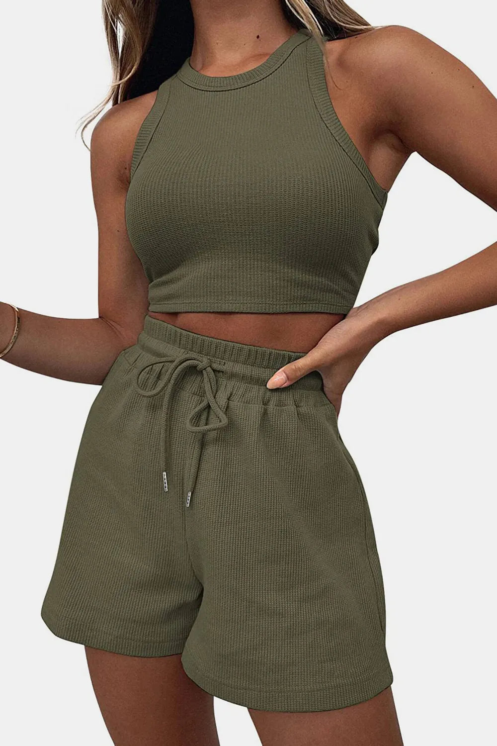 Person wearing an olive green ribbed tank top and shorts set on a plain background