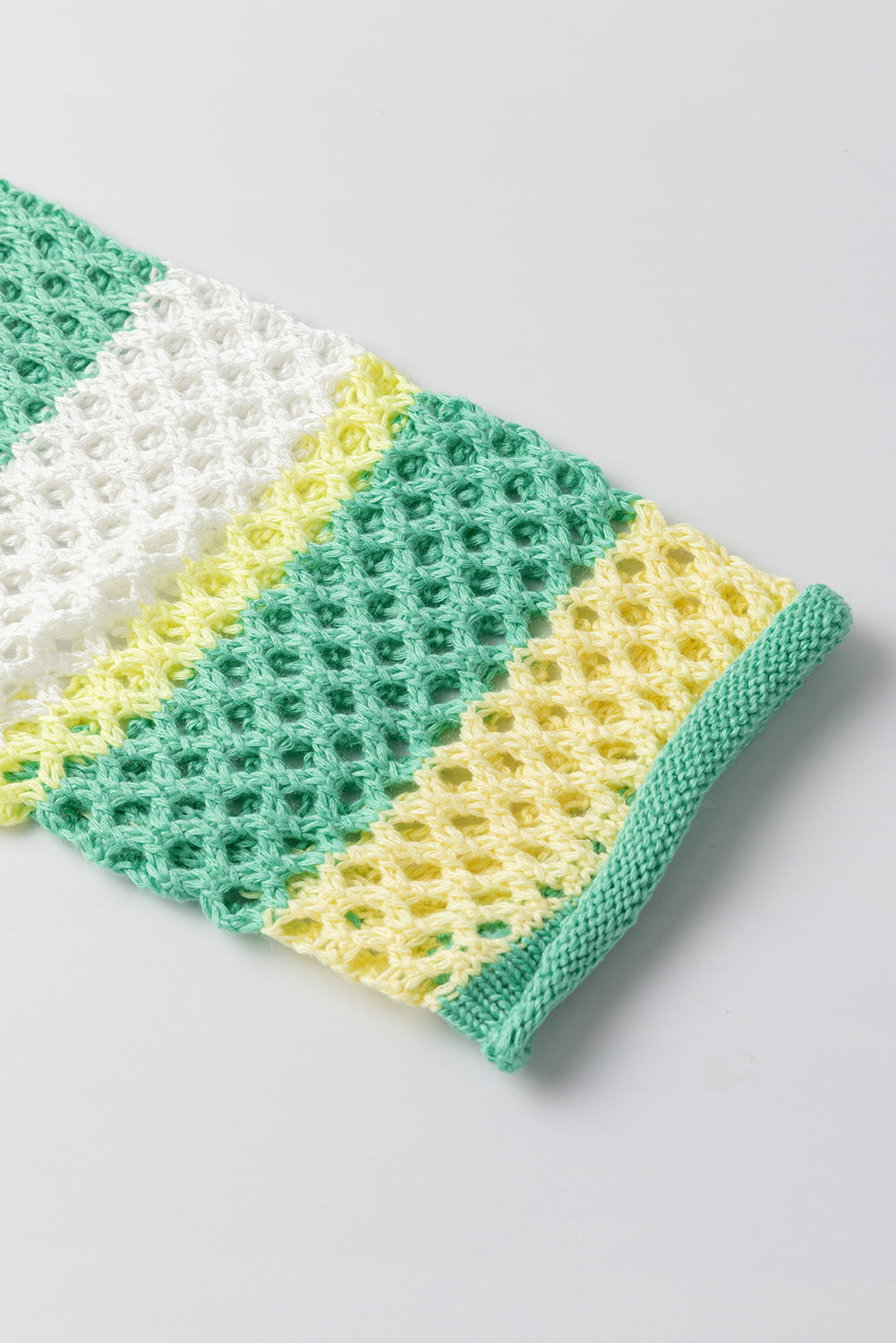 Crocheted dishcloth with green, white, and yellow pattern on a light gray background