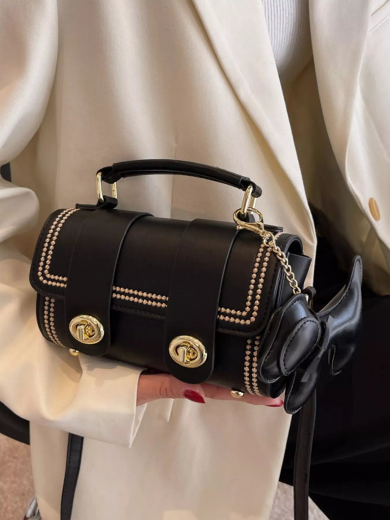 Black handbag with gold accents held by a person wearing a beige coat.