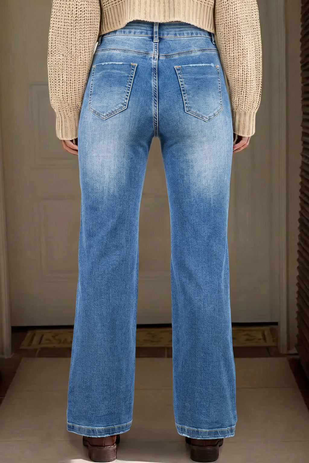 Person wearing blue jeans with a neutral background behind view