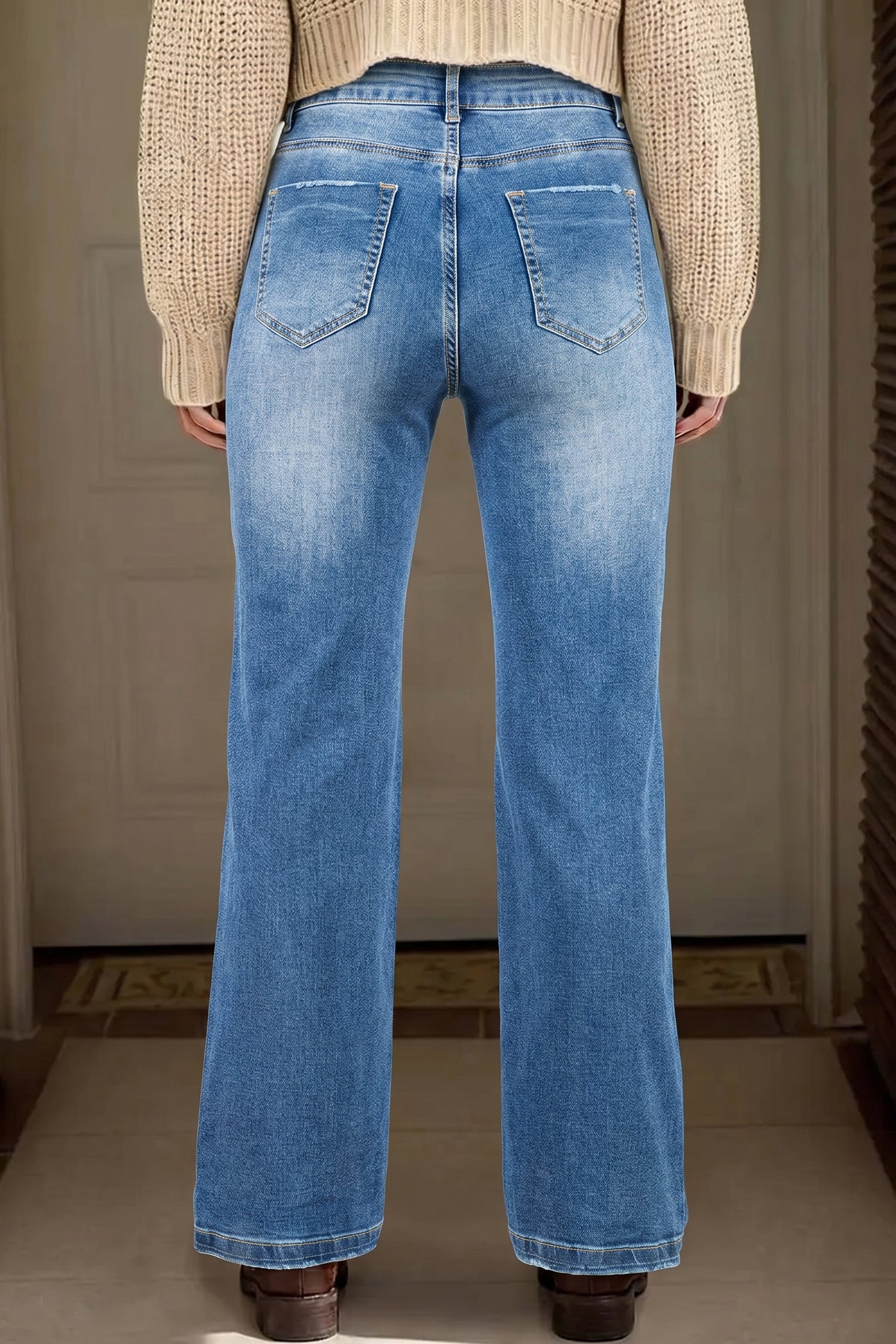 Person wearing blue jeans with a neutral background behind view