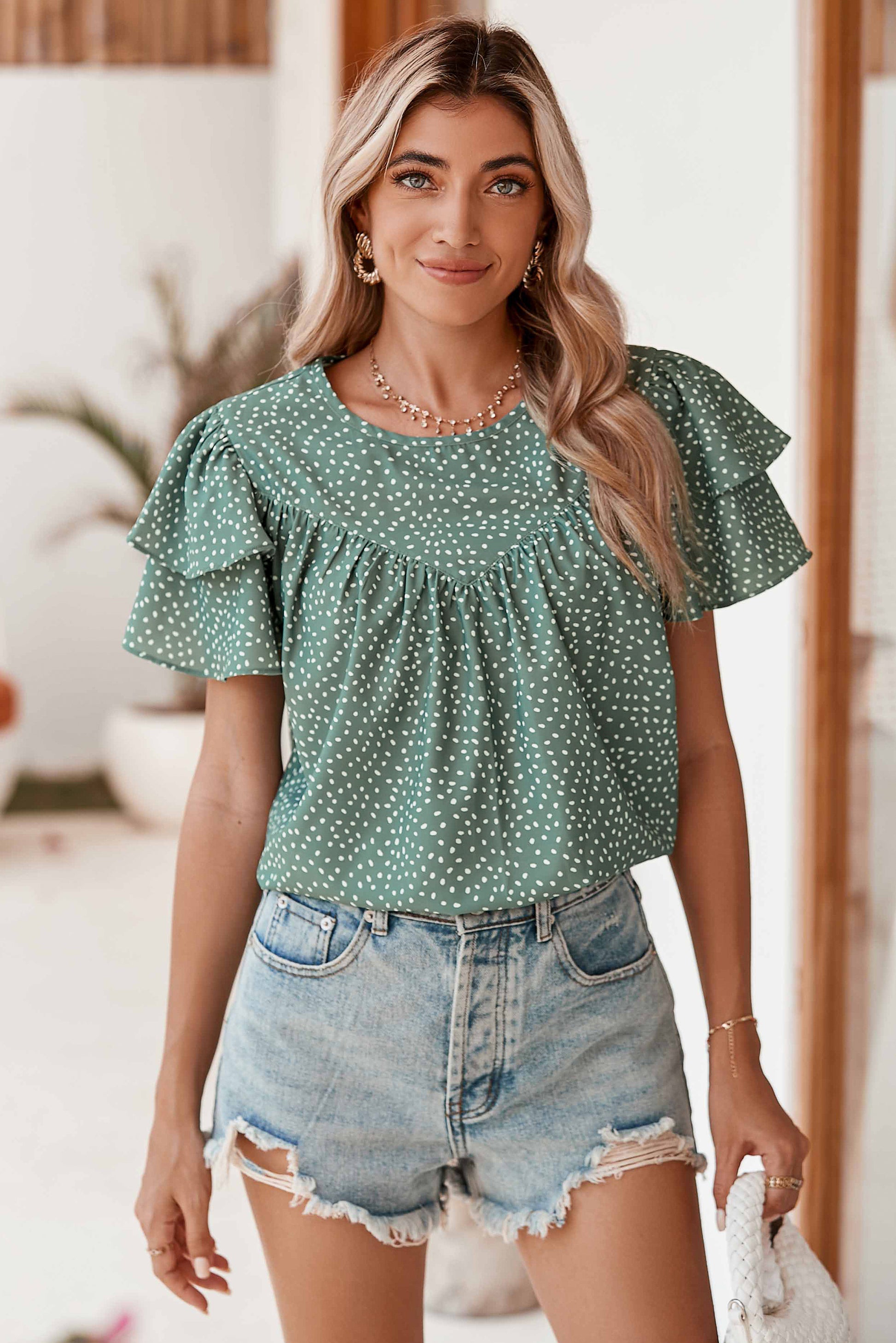 Woman wearing a green polka dot top and denim shorts outdoors.