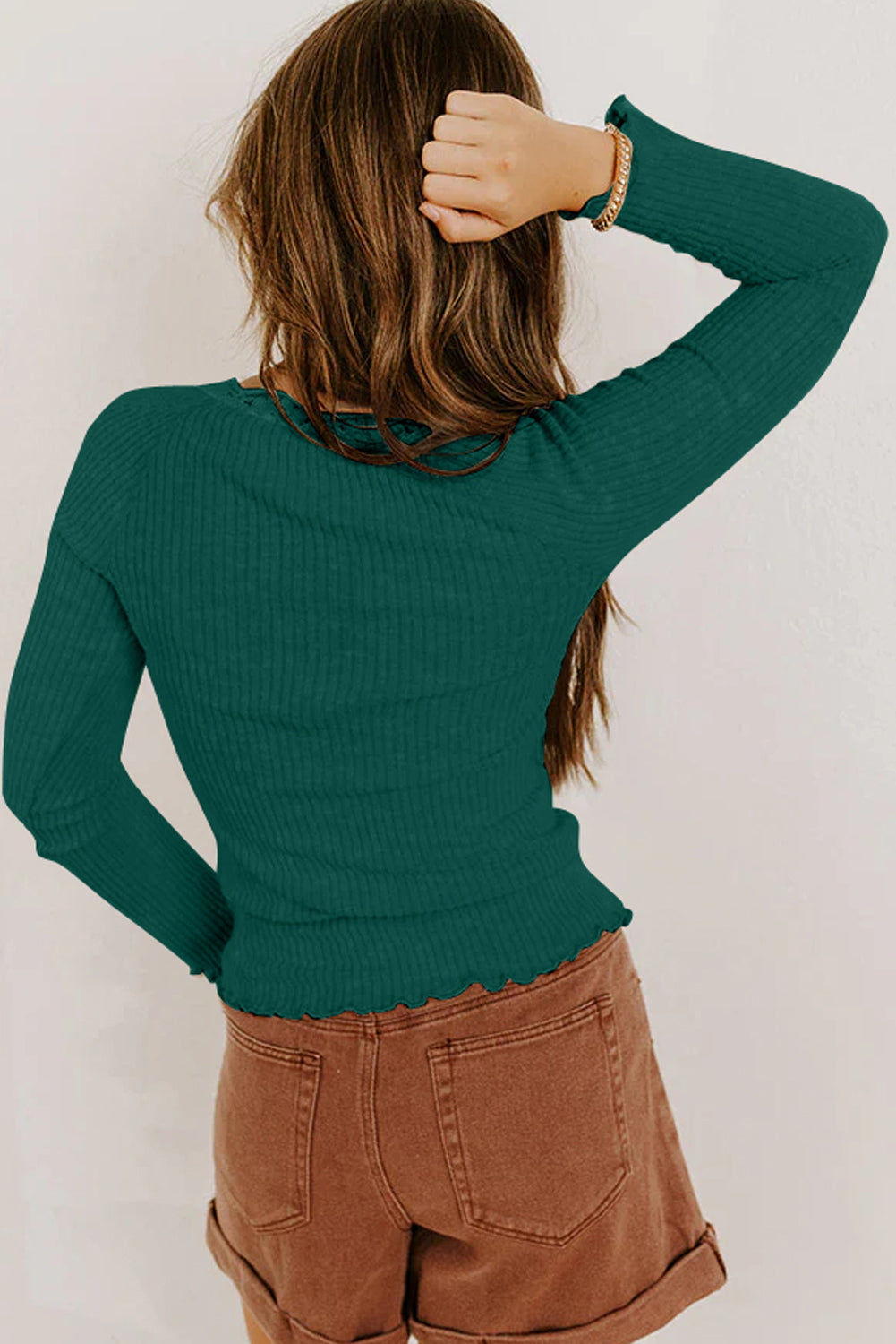 Person wearing a green ribbed sweater and brown pants against a white background