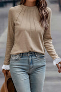 Woman wearing a beige long-sleeve top with lace cuffs and light blue jeans.
