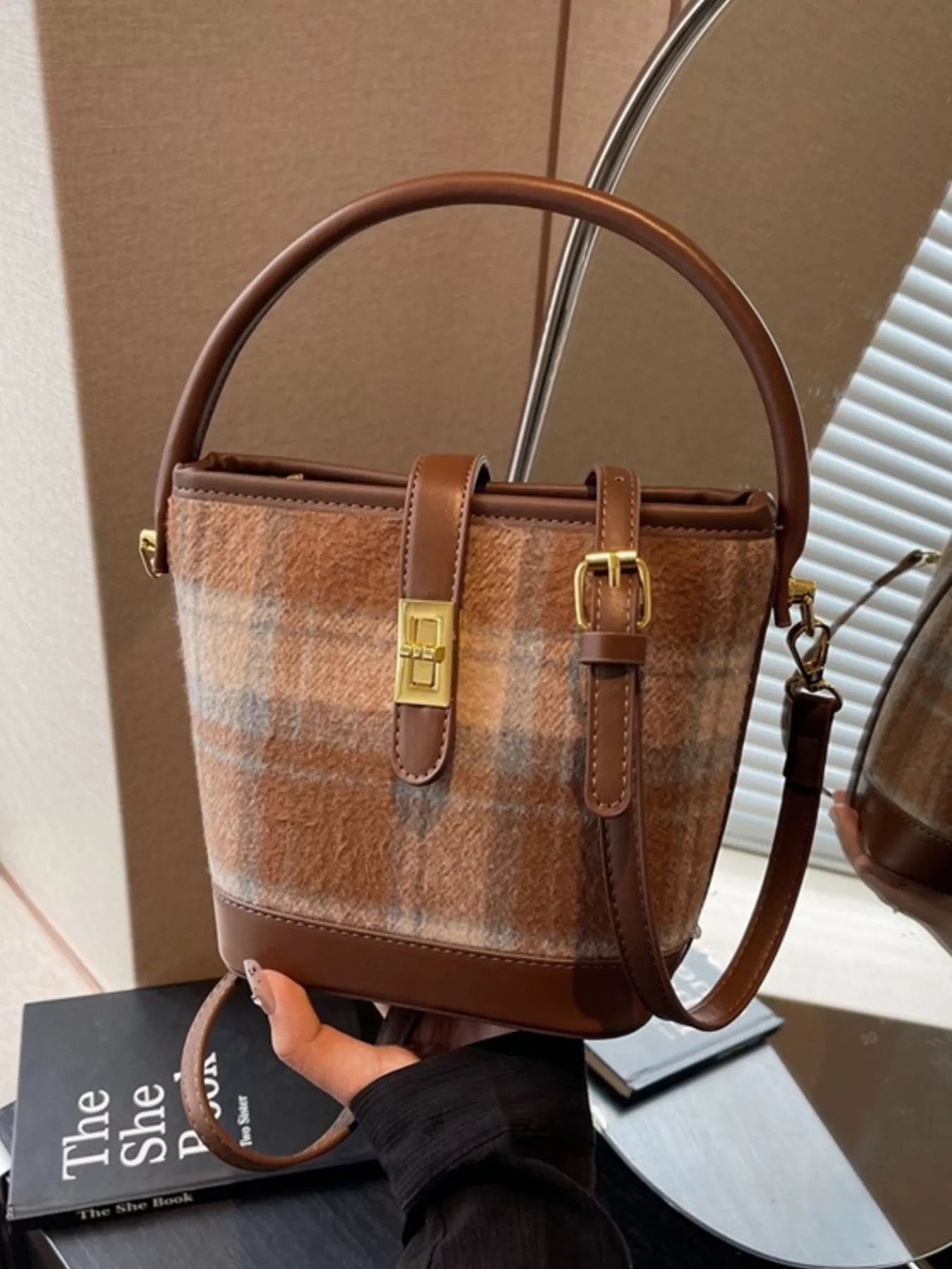 Brown plaid handbag held by a person with a book in the background