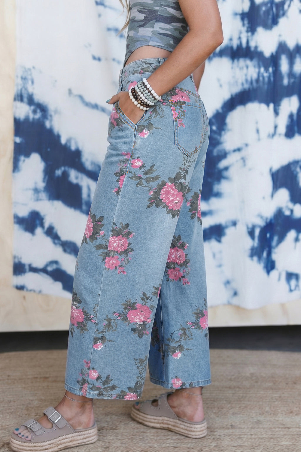 Person wearing floral denim pants with a tie-dye wall in the background angle view