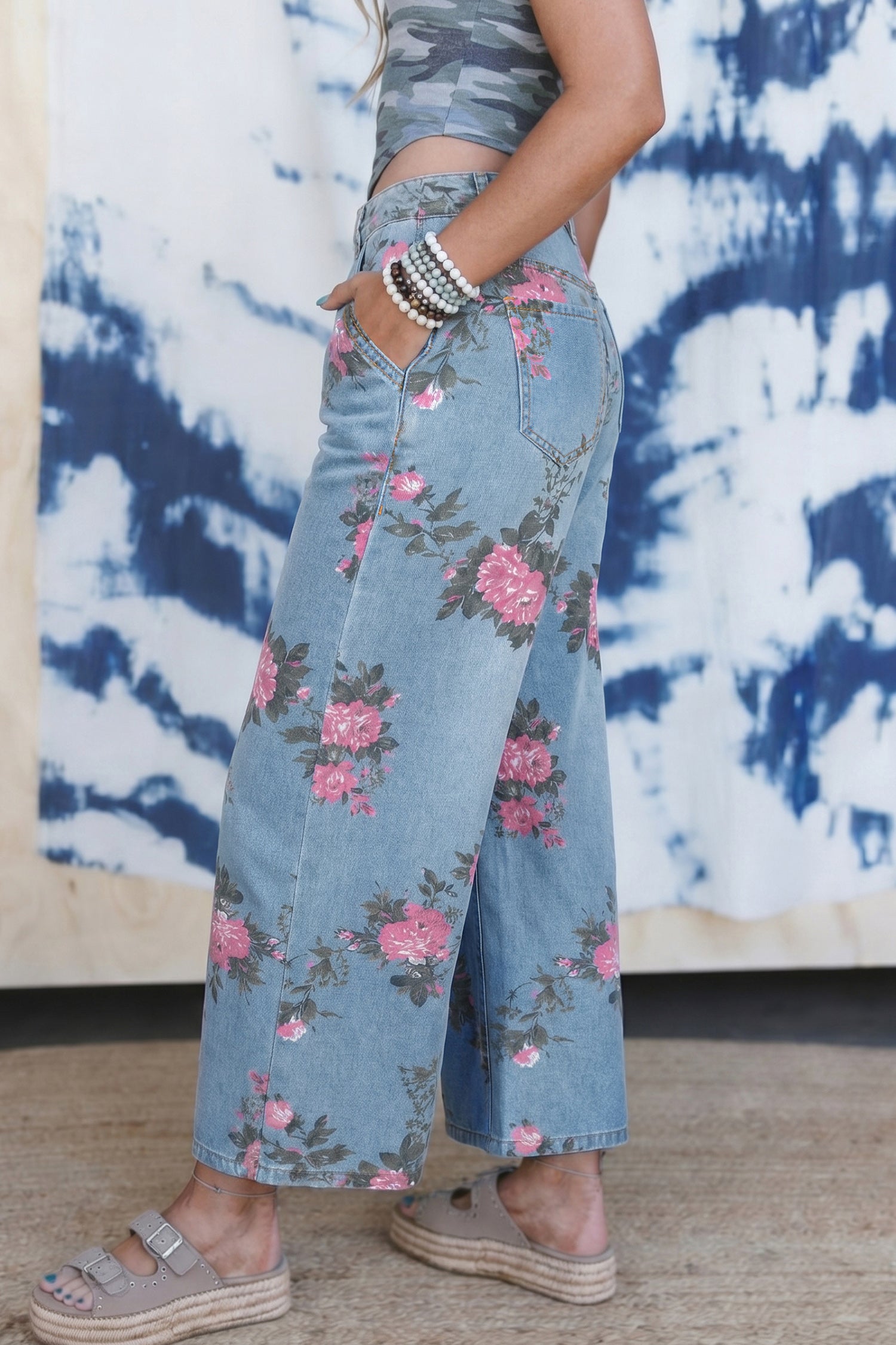 Person wearing floral denim pants with a tie-dye wall in the background angle view