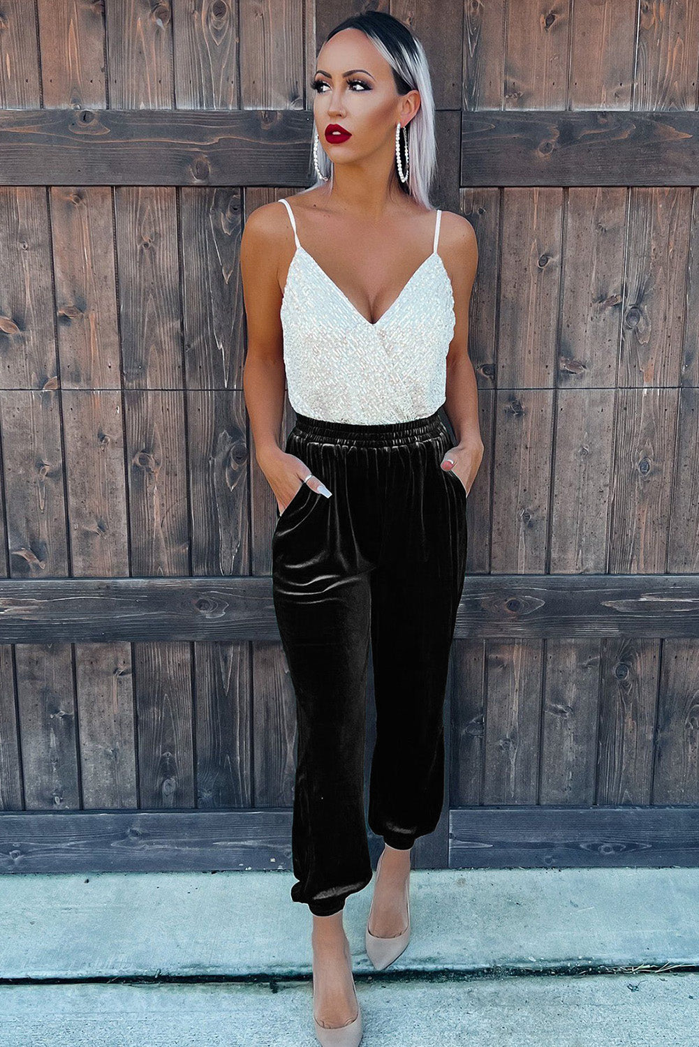 Woman wearing a white lace top and black pants standing against a wooden fence.