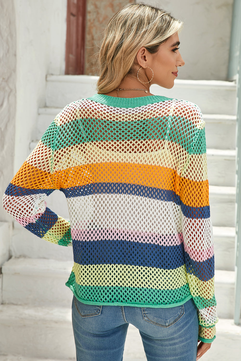 Woman wearing a colorful striped mesh sweater on a staircase.