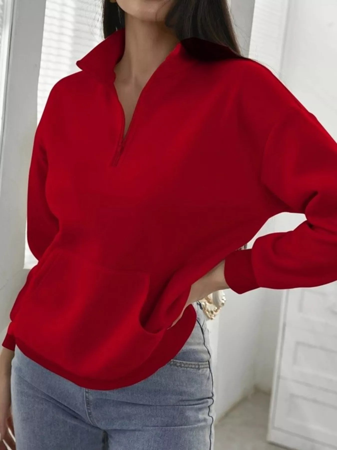 Person wearing a red sweater and light blue jeans indoors.