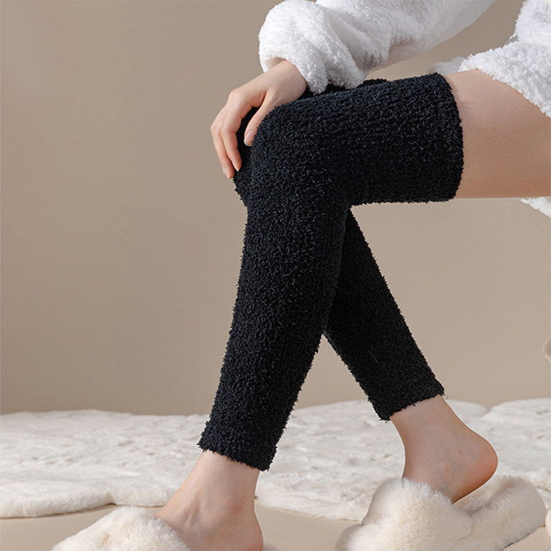Person wearing black fuzzy leggings sitting on a white surface with a neutral background