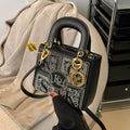 Black handbag with gold accents and a visible brand logo on a beige surface.