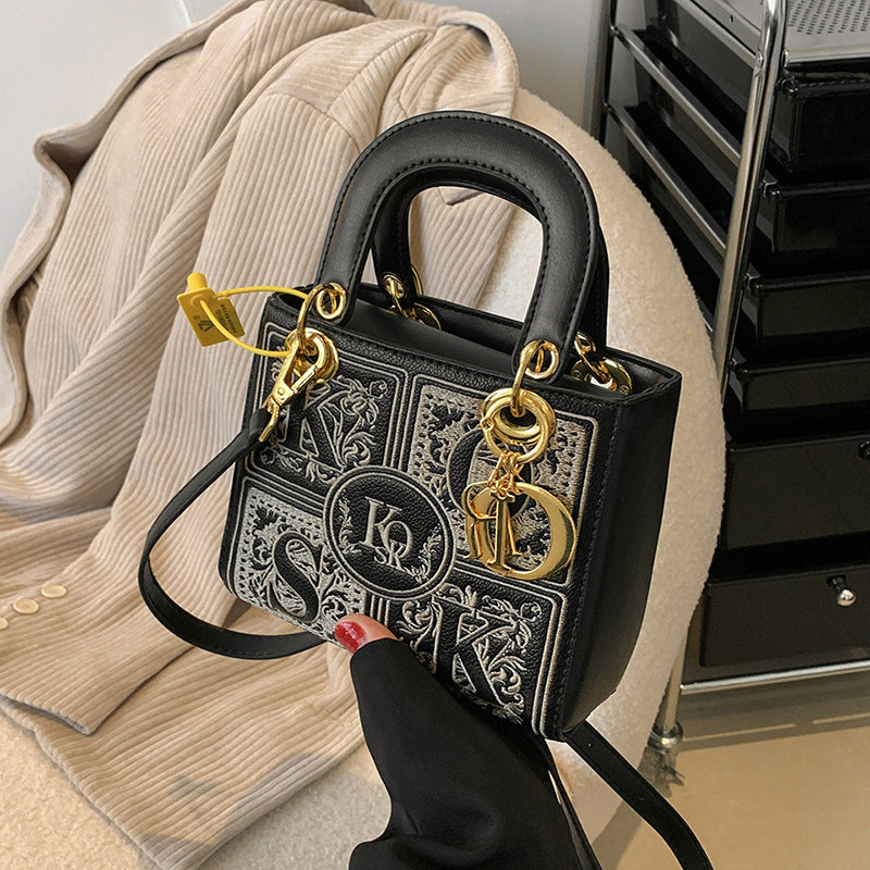 Black handbag with gold accents and a visible brand logo on a beige surface.