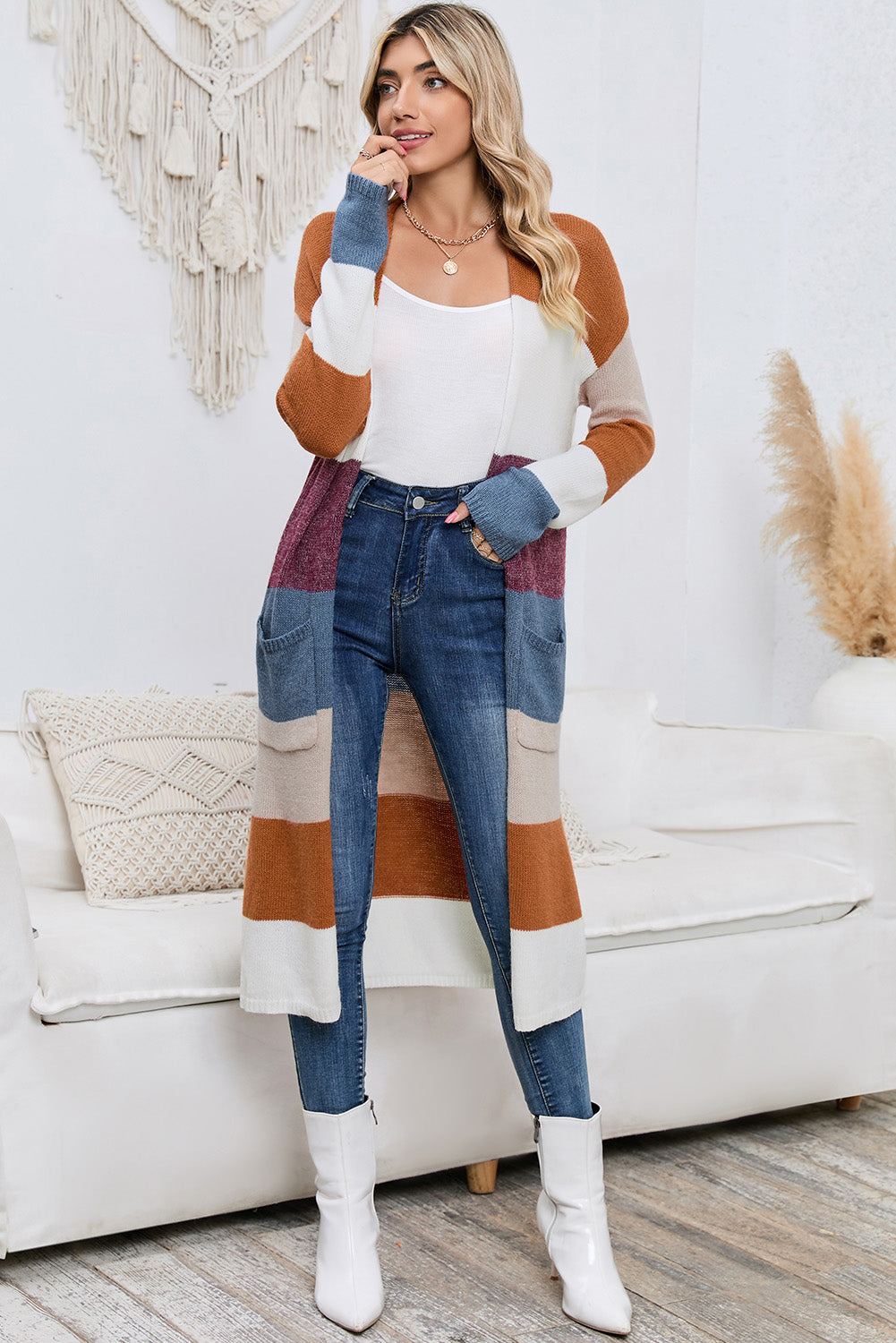 Woman wearing a colorful sweater, white top, blue jeans, and white boots in a living room setting.