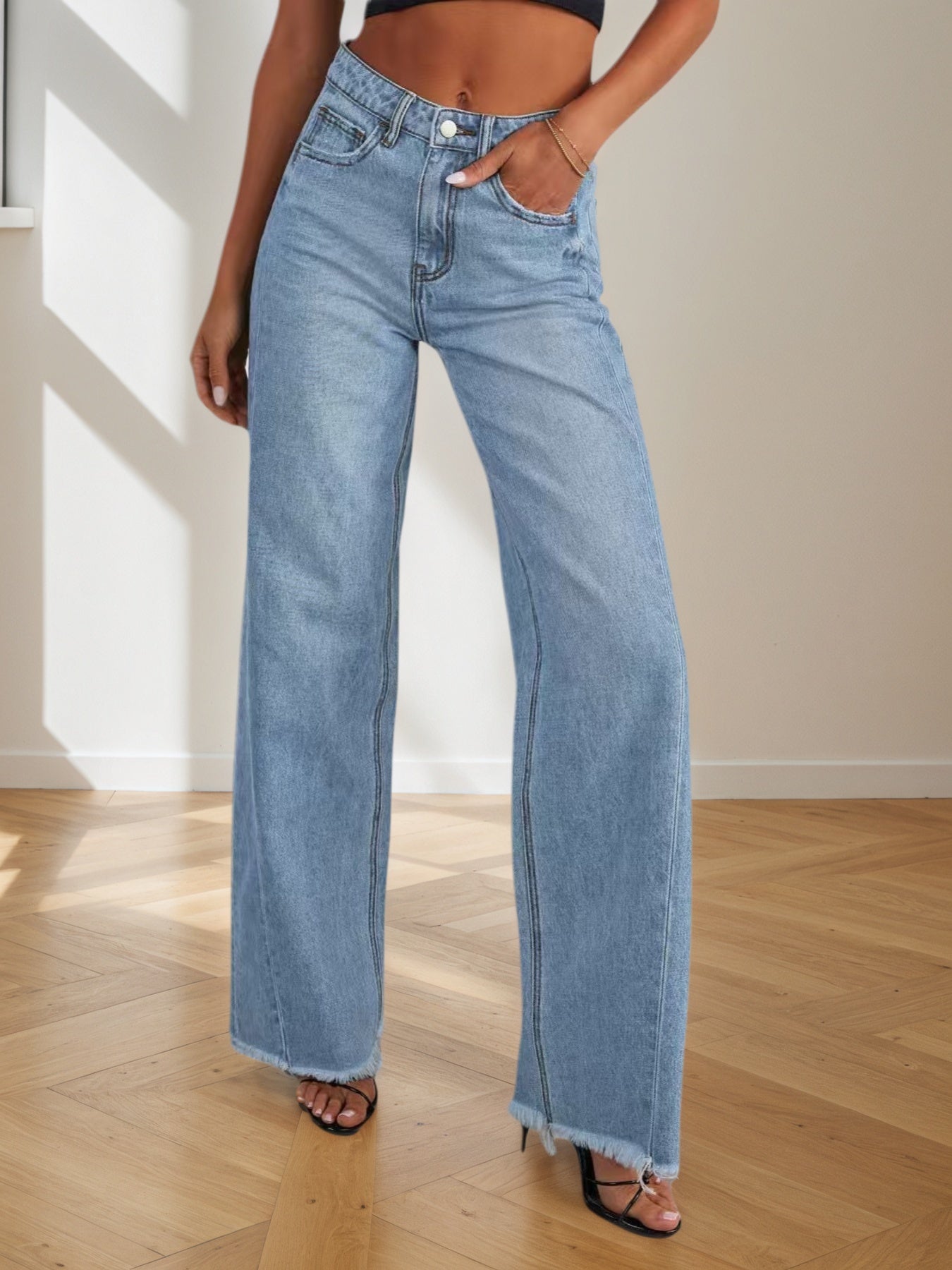 Person wearing light blue jeans standing on a wooden floor with a neutral background