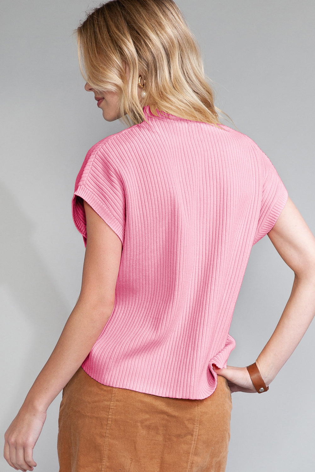 Woman wearing a pink ribbed top against a gray background