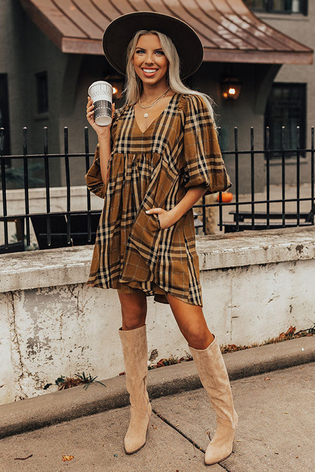 Woman in plaid dress and beige boots holding a coffee cup outdoors.