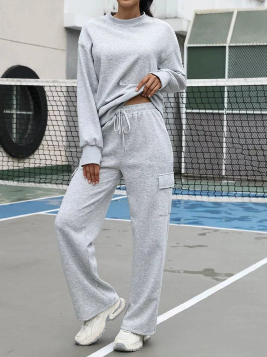 Person wearing a gray sweatshirt and pants on a tennis court