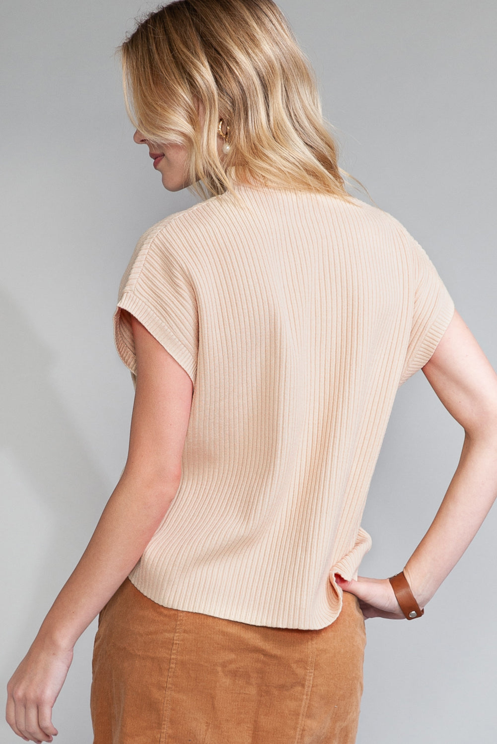 Woman wearing a beige ribbed top and brown pants against a gray background