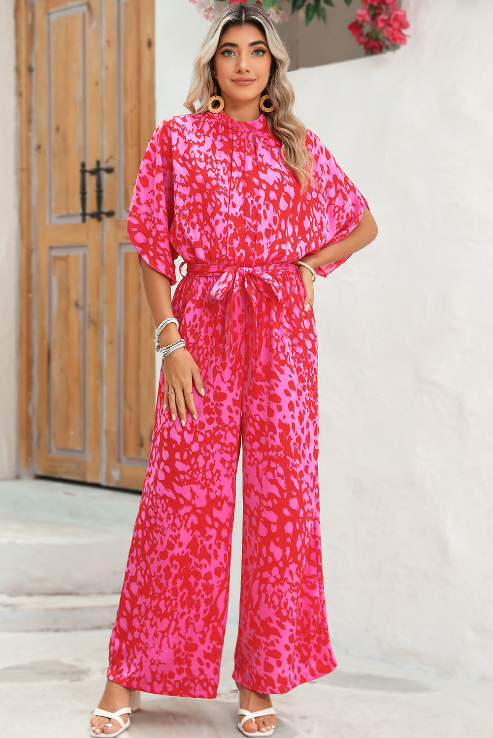 Woman wearing a bright pink patterned jumpsuit standing in front of a wooden door.