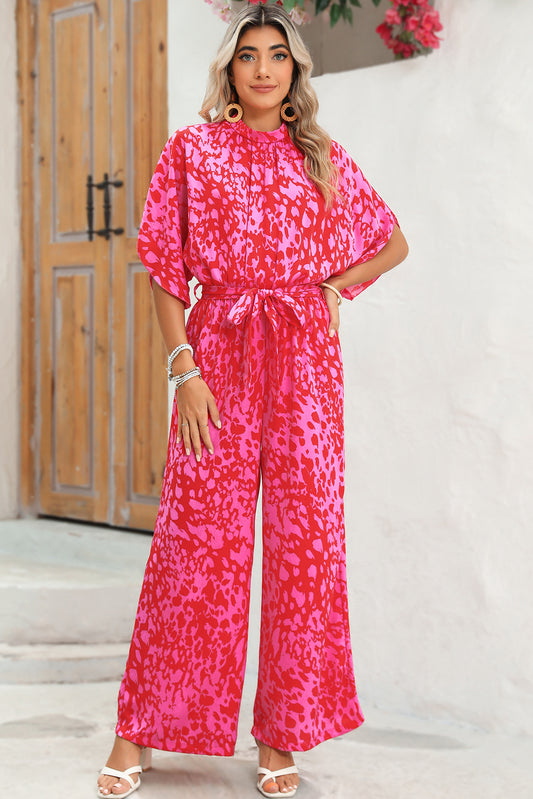 Woman wearing a bright pink patterned jumpsuit standing in front of a wooden door.