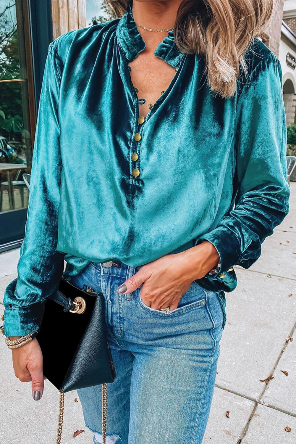 Person wearing a teal velvet shirt and blue jeans, holding a black handbag.
