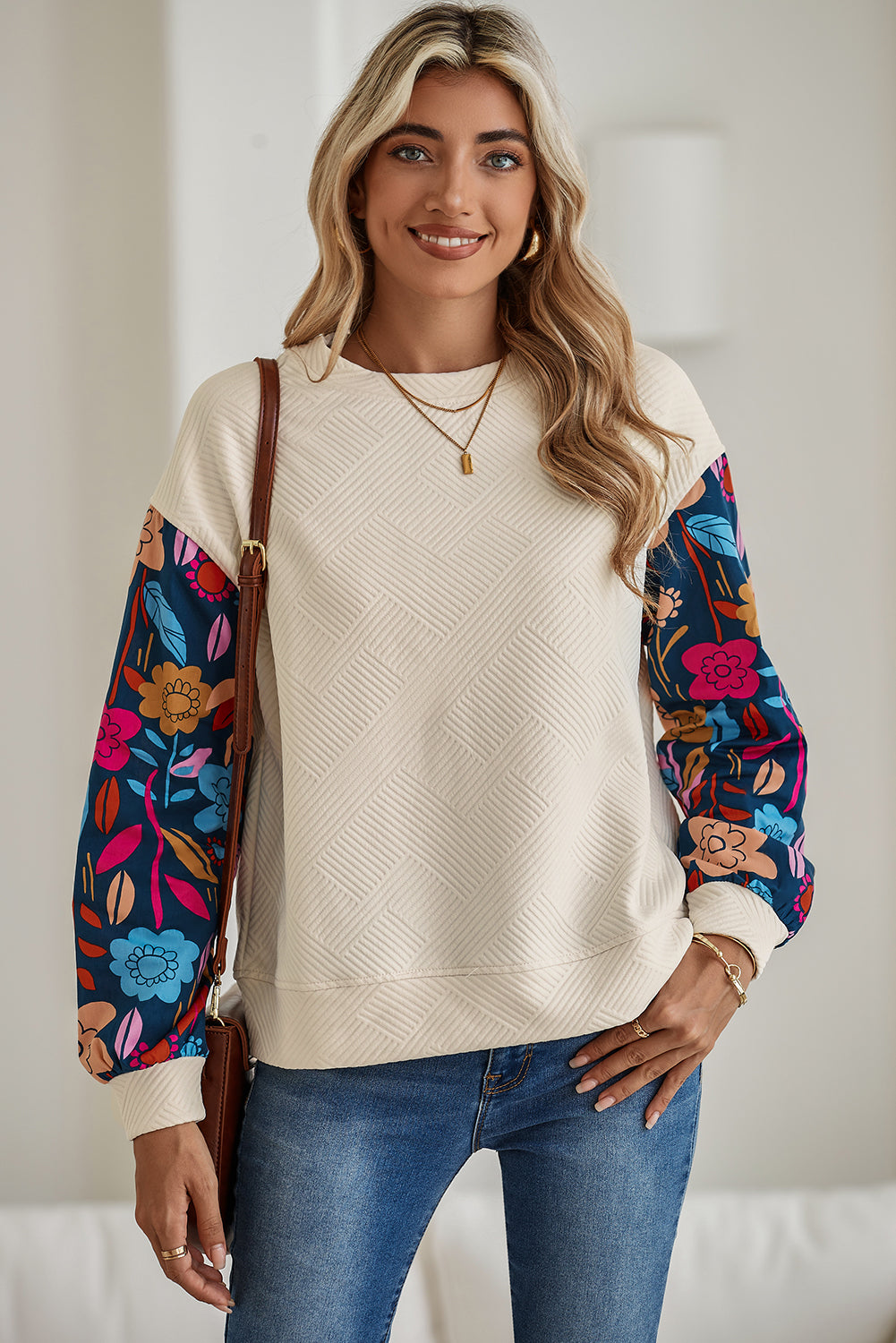 Woman wearing a cream sweater with colorful floral sleeves and blue jeans indoors.