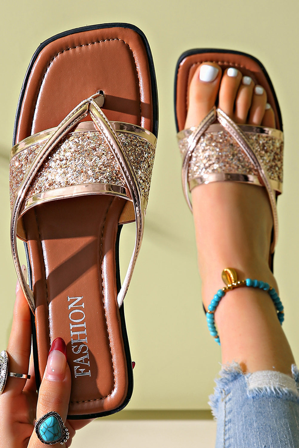 Brown sandals with glittery straps worn by a person against a light green background