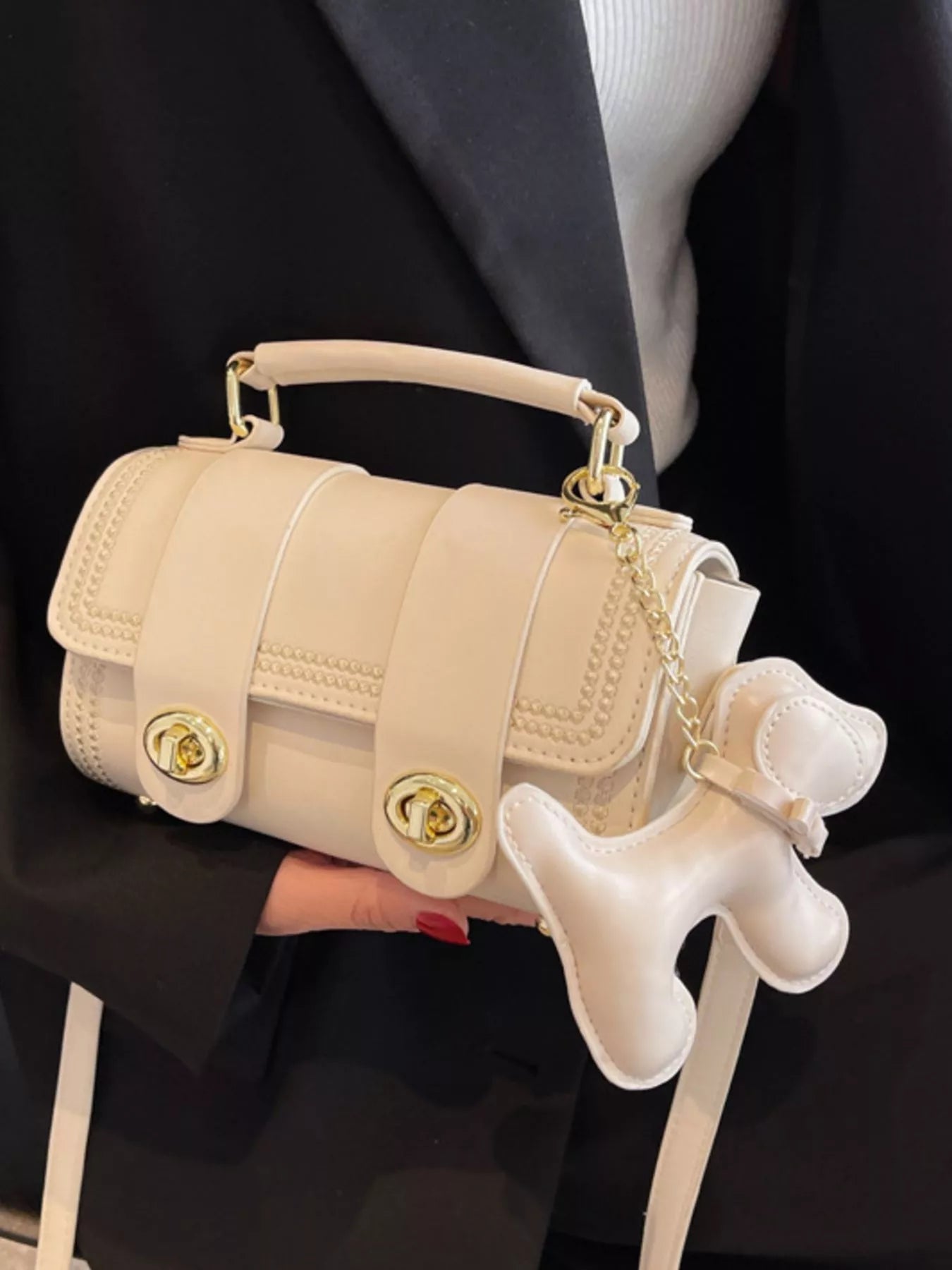 Beige handbag with a dog-shaped charm held by a person against a black background