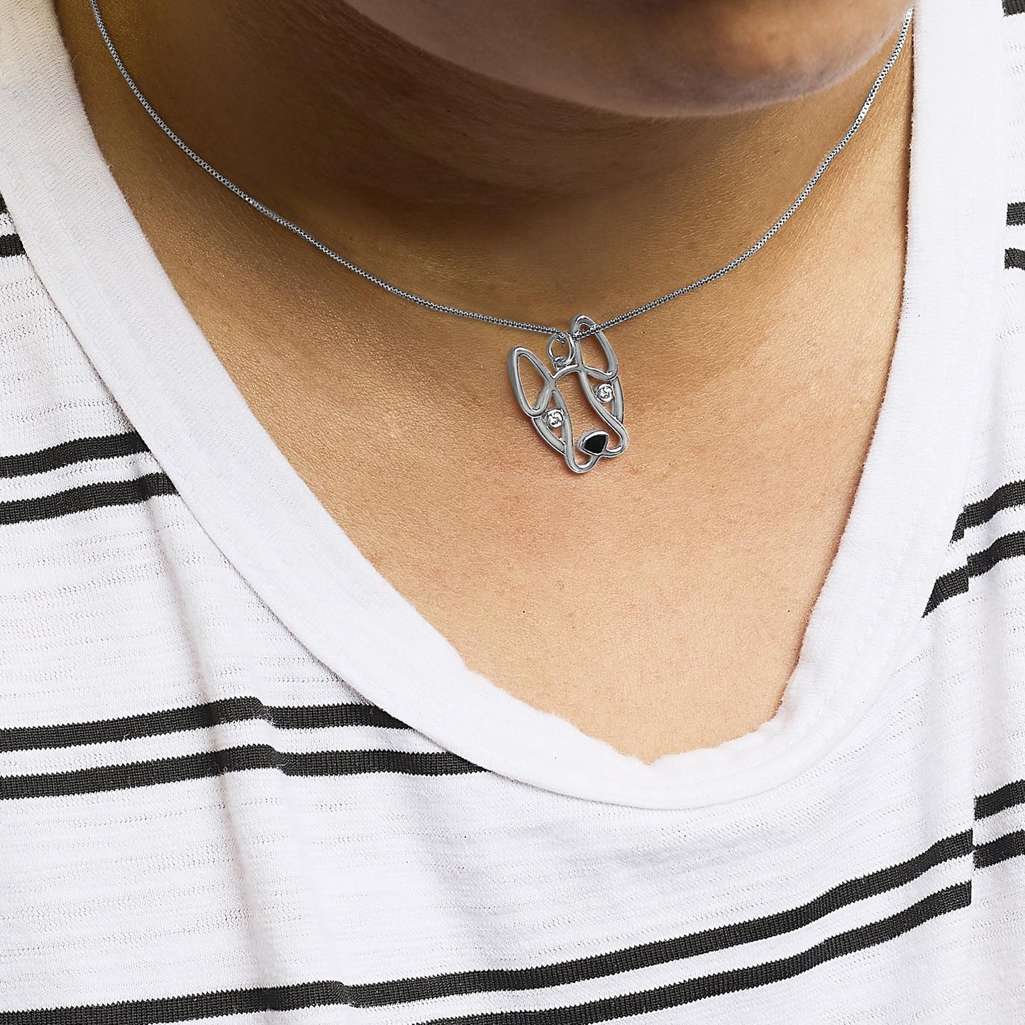 Silver dog-shaped pendant necklace on a person wearing a white and black striped shirt.