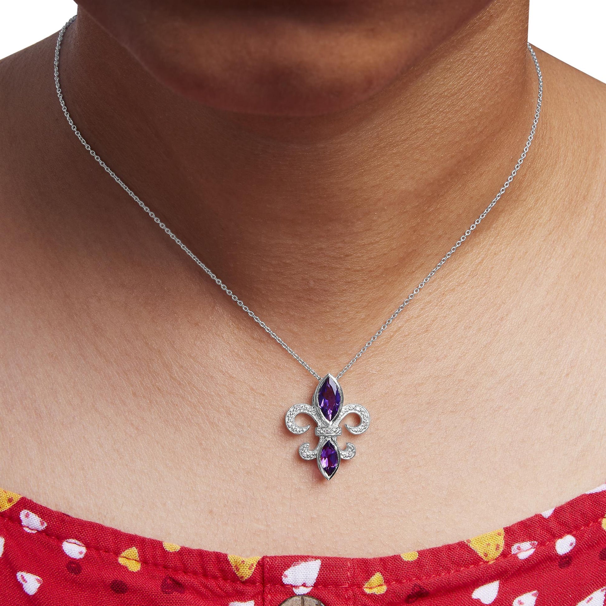 Necklace with a fleur-de-lis pendant on a person wearing a red top with white and yellow patterns.