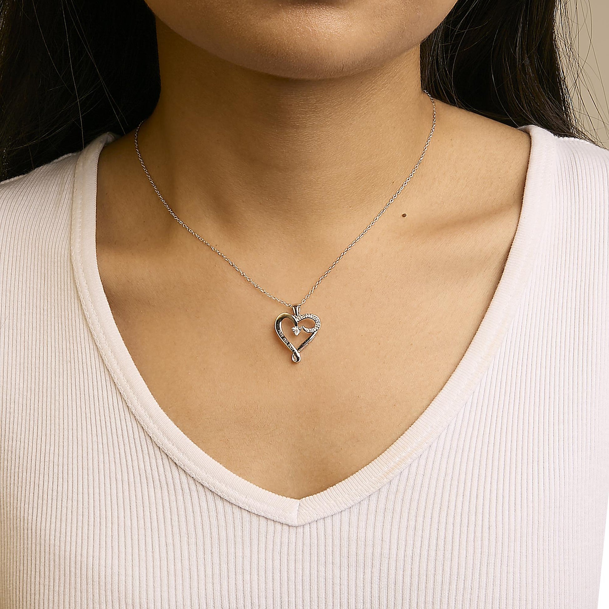 Silver heart-shaped necklace worn by a person in a white top